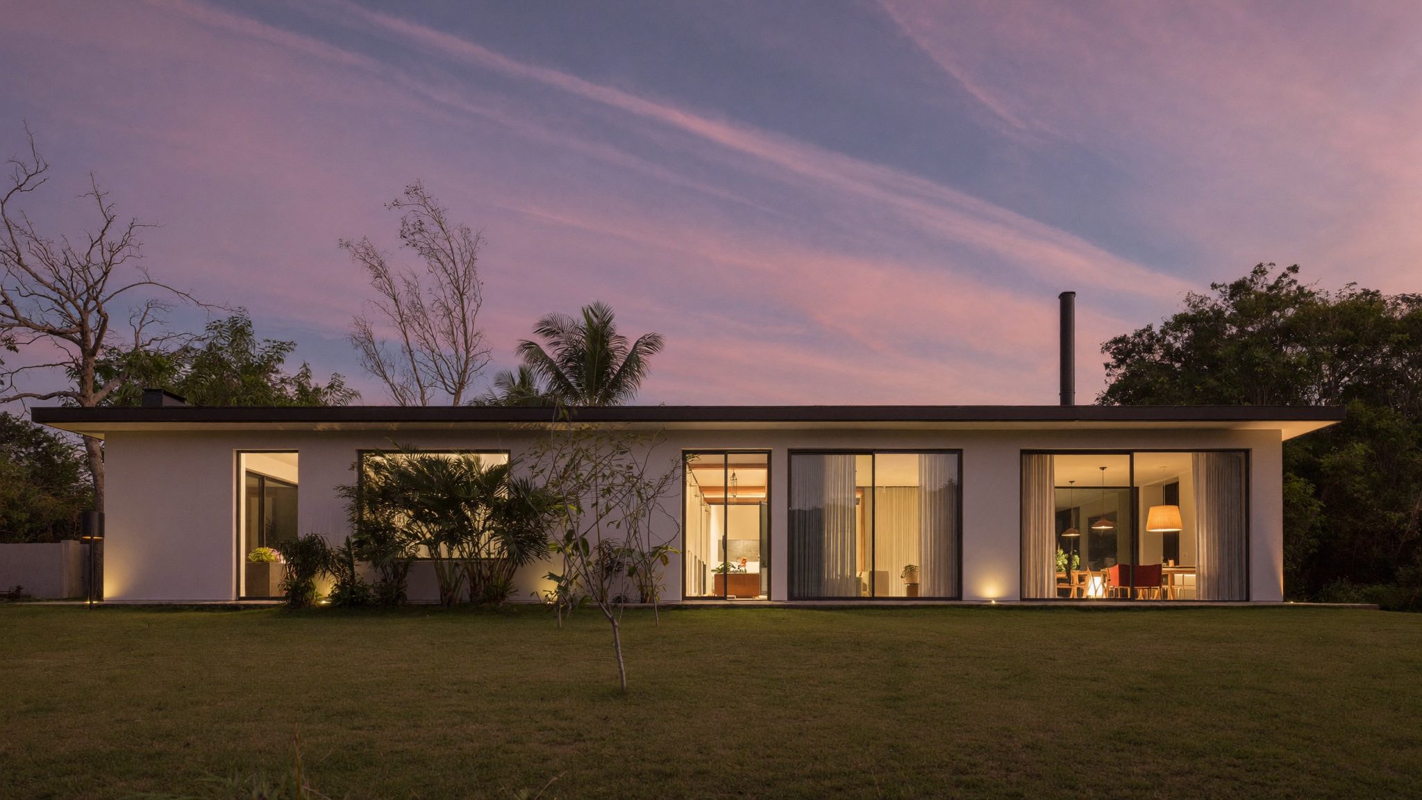 Rumah tropis modern saat senja dengan pencahayaan hangat